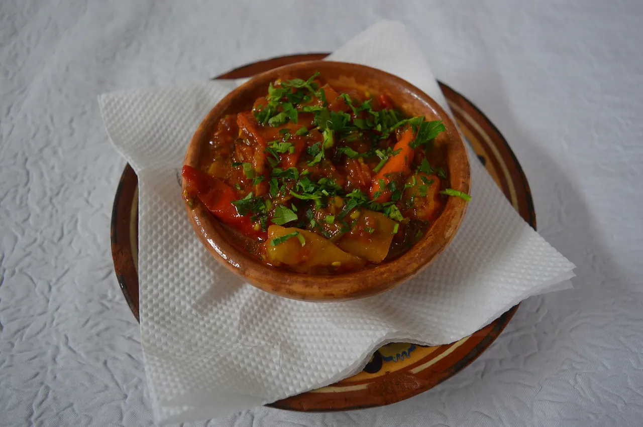 A clay bowl of chunky pindjur with pieces of pepper and tomato, topped with chopped parsley