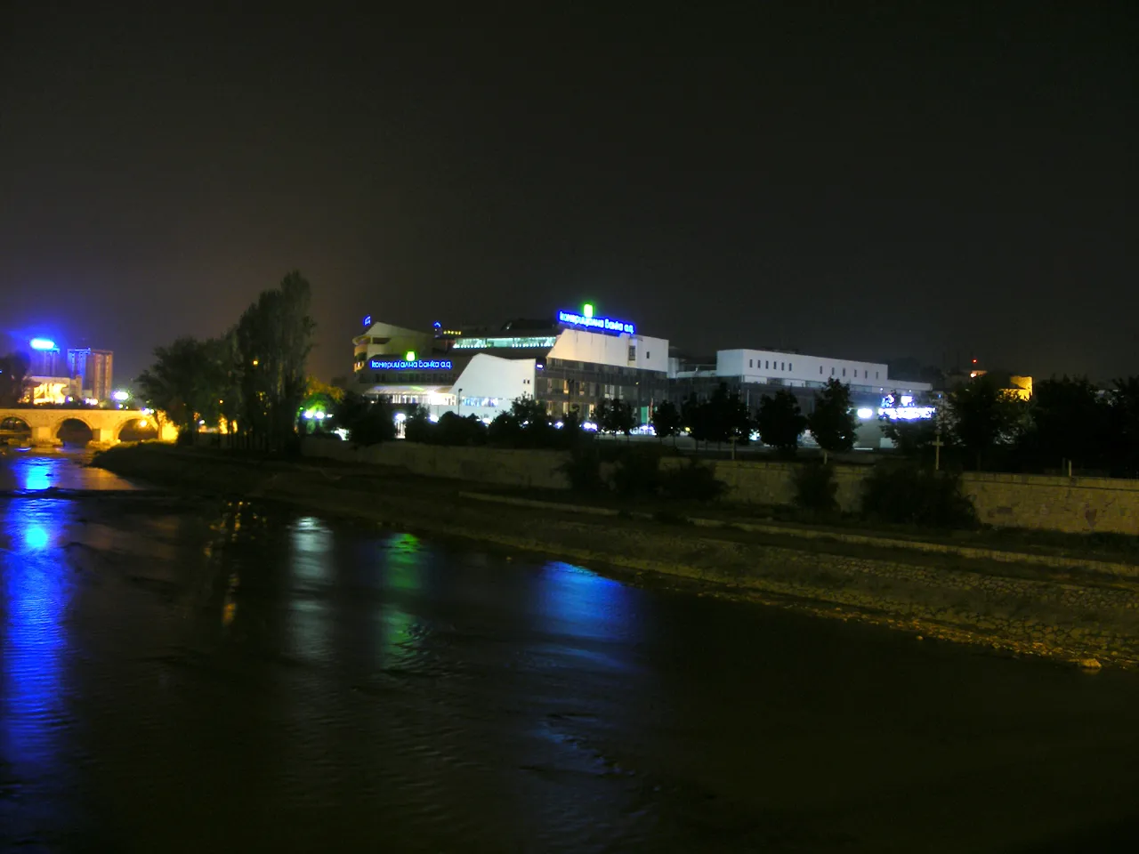 The illuminated Komercijalna Banka headquarters building on the Vardar riverbank in Skopje at night