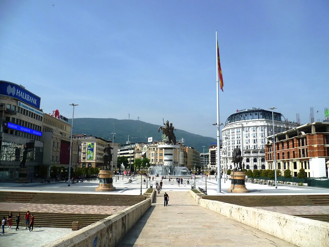 Macedonia Square in Skopje with the Alexander the Great monument, fountains, and a Halkbank sign on a building to the left