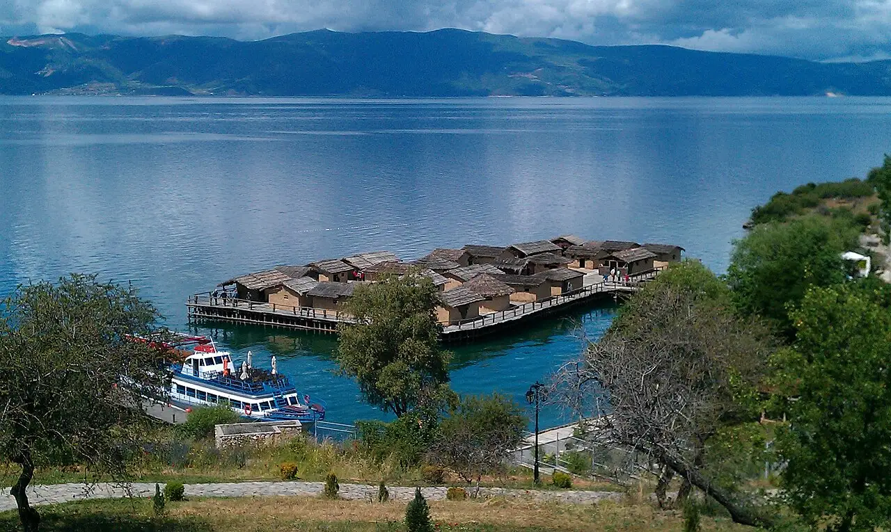 The reconstructed pile-dwelling village of the Bay of Bones on stilts over Lake Ohrid, an excursion boat moored alongside