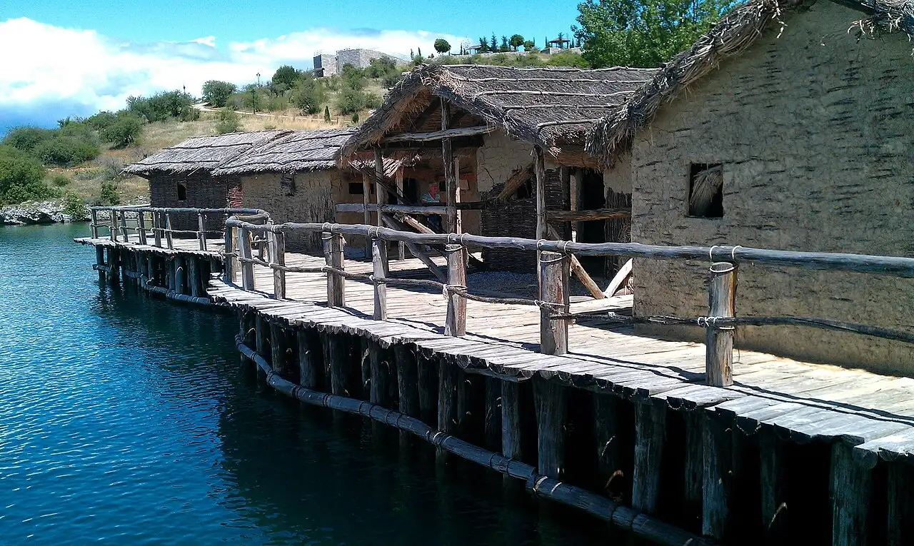 A wooden boardwalk with rustic railings running past reed-roofed mud houses of the Bay of Bones over the water