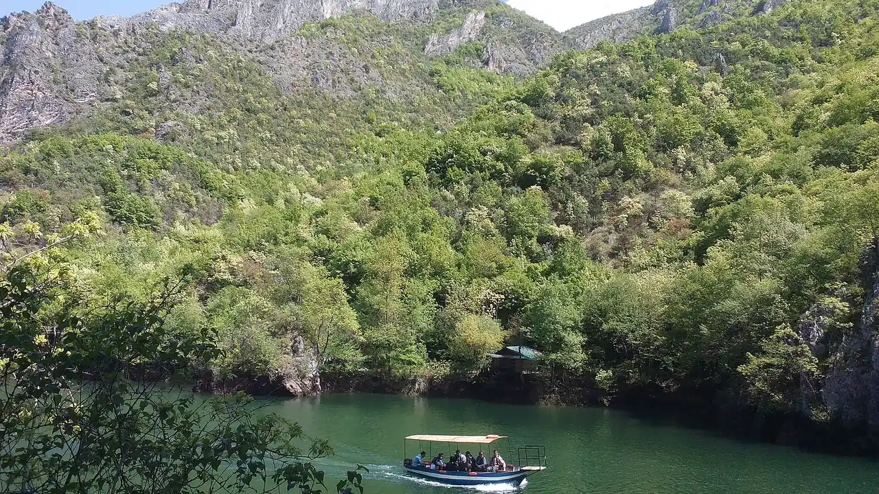 A small tour boat on the green Treska river between the steep cliffs of Matka Canyon near Skopje