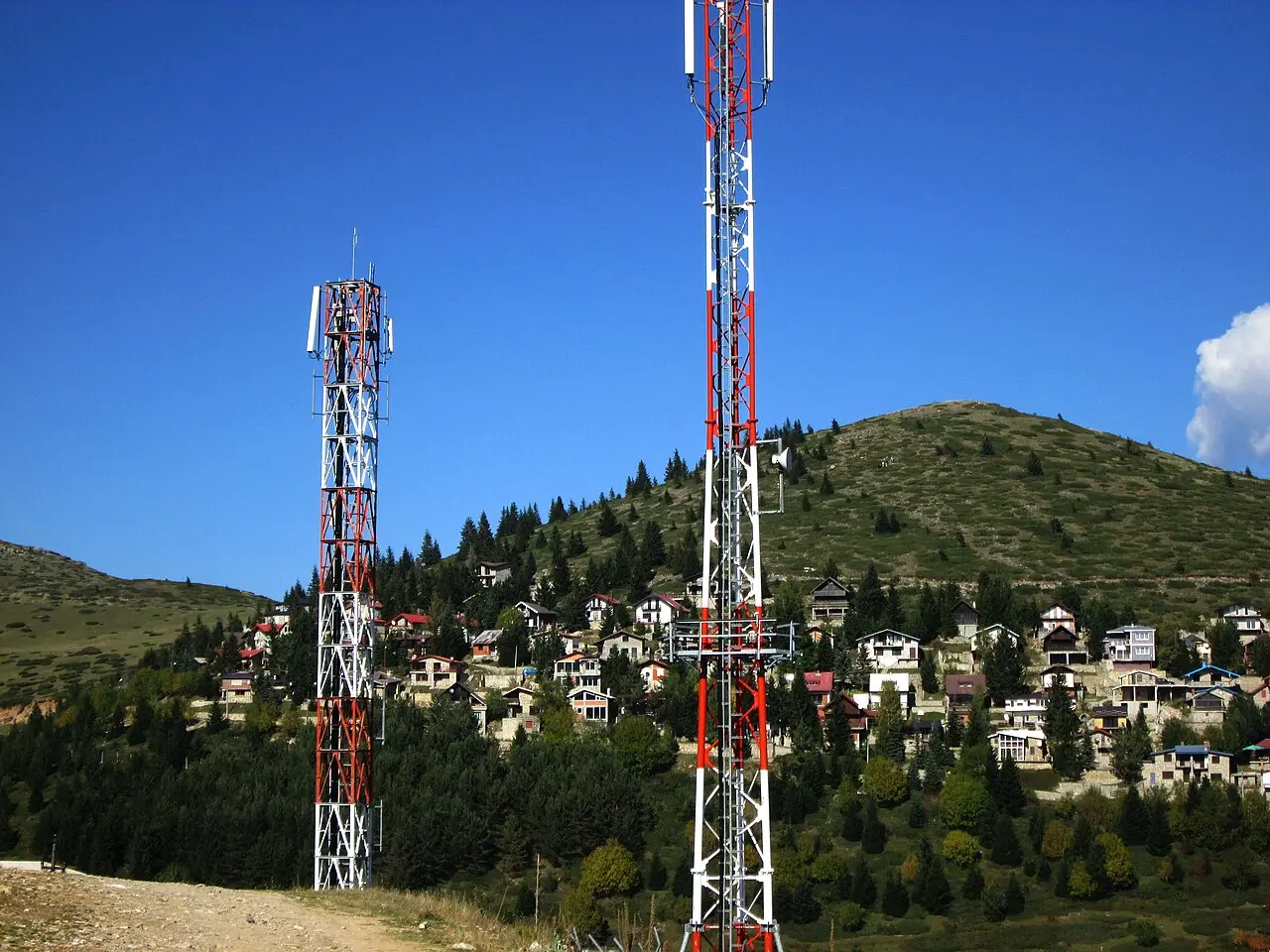 Two mobile masts on a hillside above a village of stone houses in the Macedonian mountains