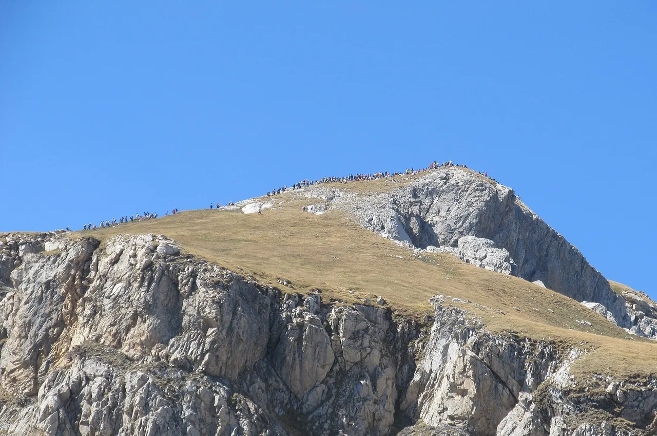 A long line of hikers on the broad summit ridge of Mount Korab, the highest peak in North Macedonia