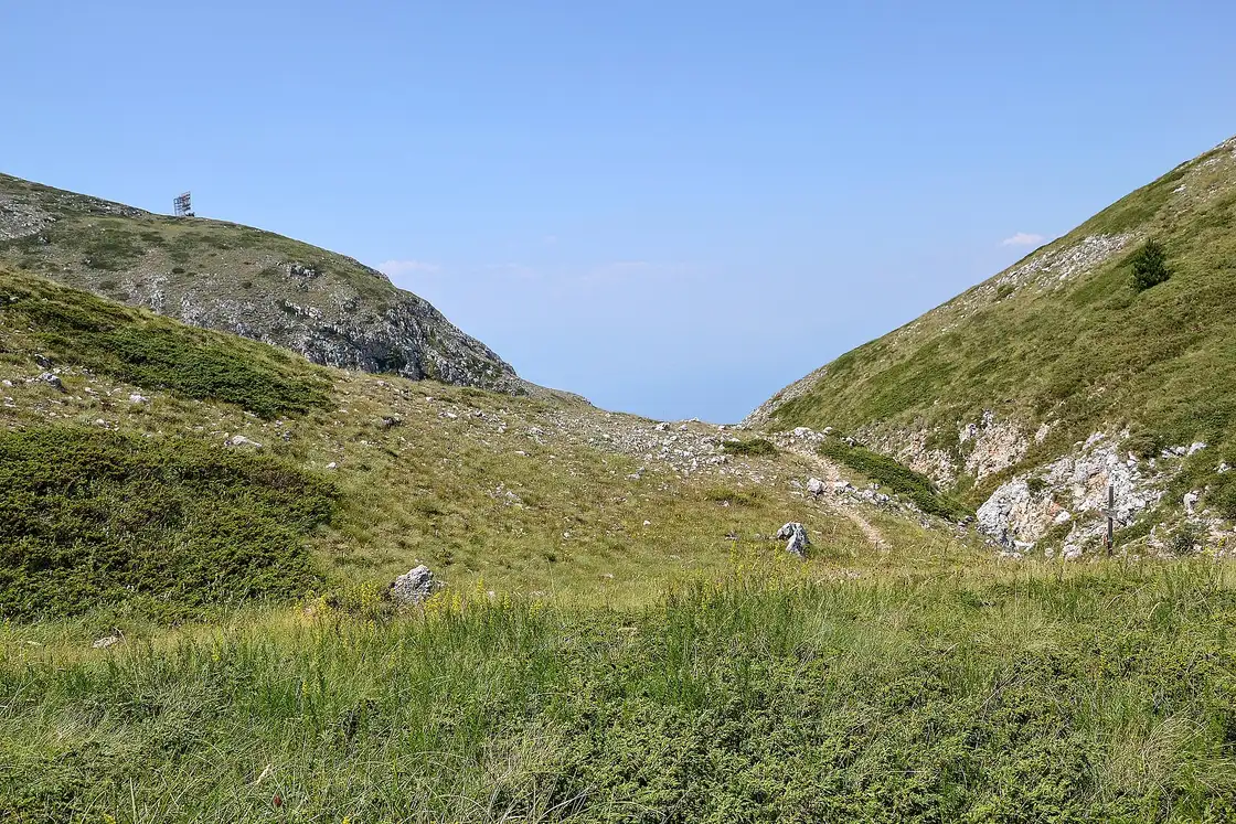 A grassy hiking trail climbing through a shallow valley toward the ridge of Galičica near Magaro