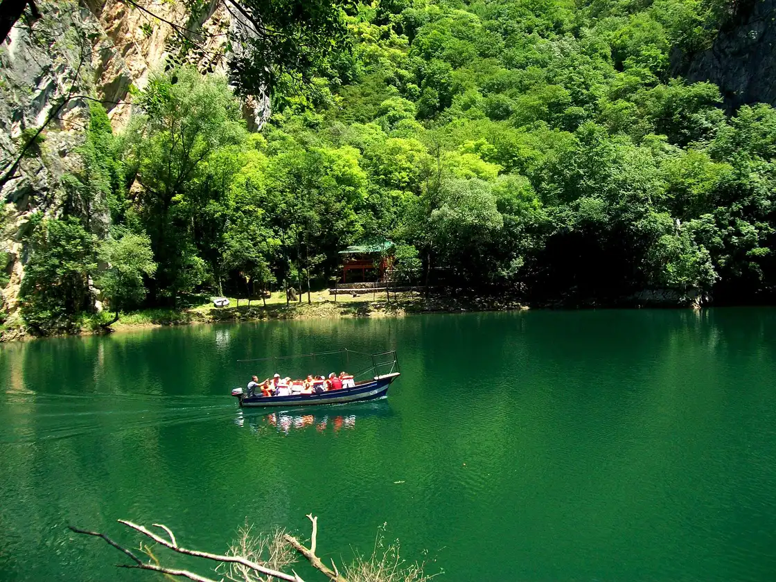 A tour boat on the emerald reservoir of Matka Canyon below wooded cliffs