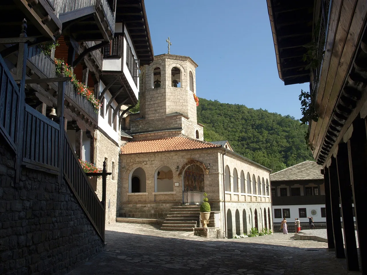 The stone church with its arcaded porch and separate bell tower, framed by the wooden balconies of the monastery lodgings