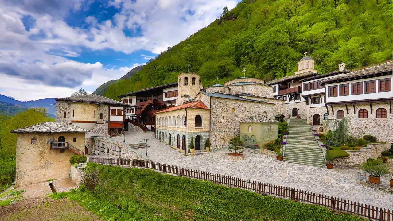 The white and stone buildings of Bigorski Monastery spread along a ledge below a forested mountainside