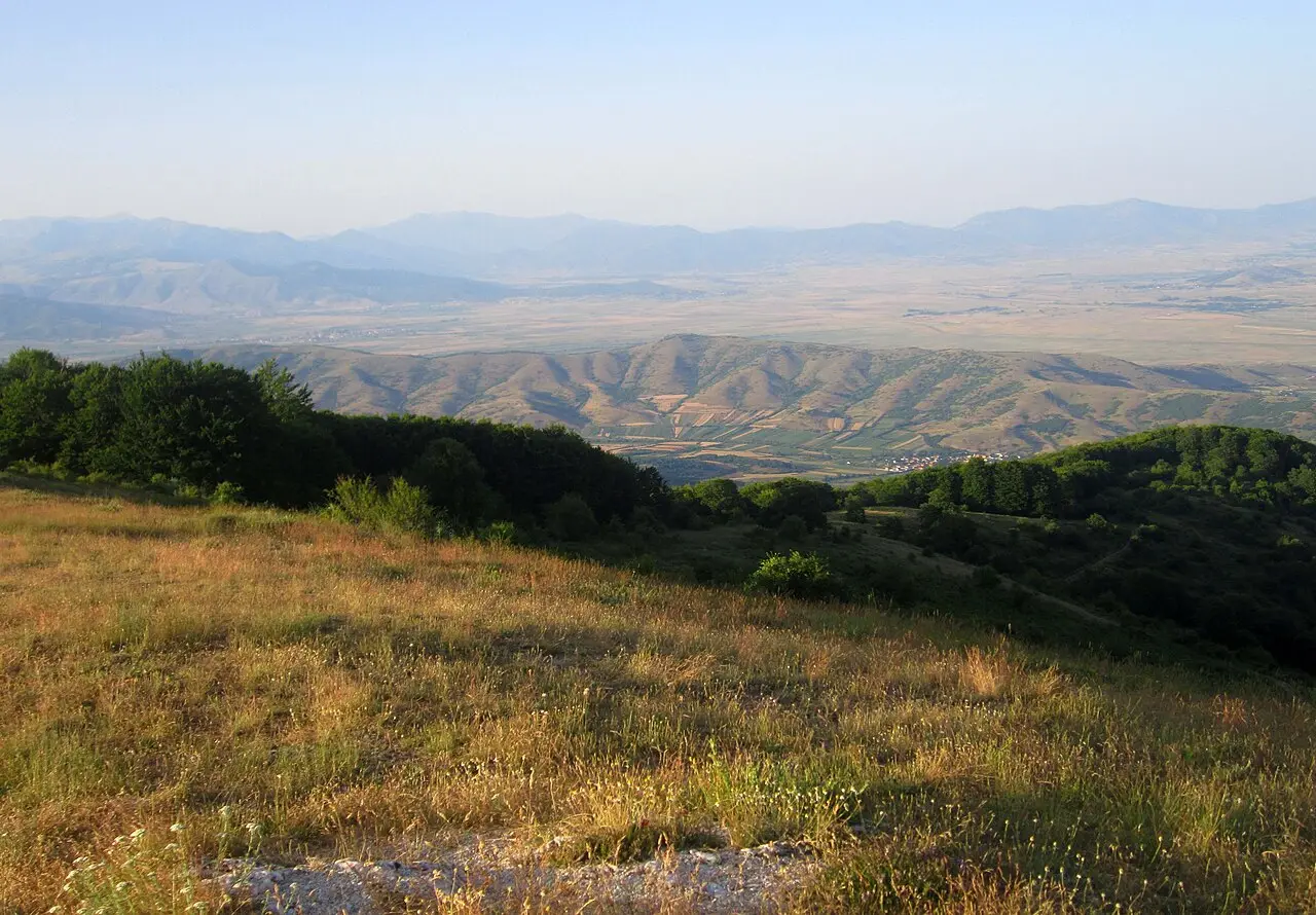 A grassy hillside overlooking the flat farmland of the Pelagonia plain that the Bitola-Prilep road crosses