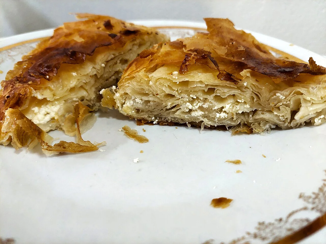 A cheese burek cut open on a plate, showing thin layers of pastry with crumbled white cheese between them
