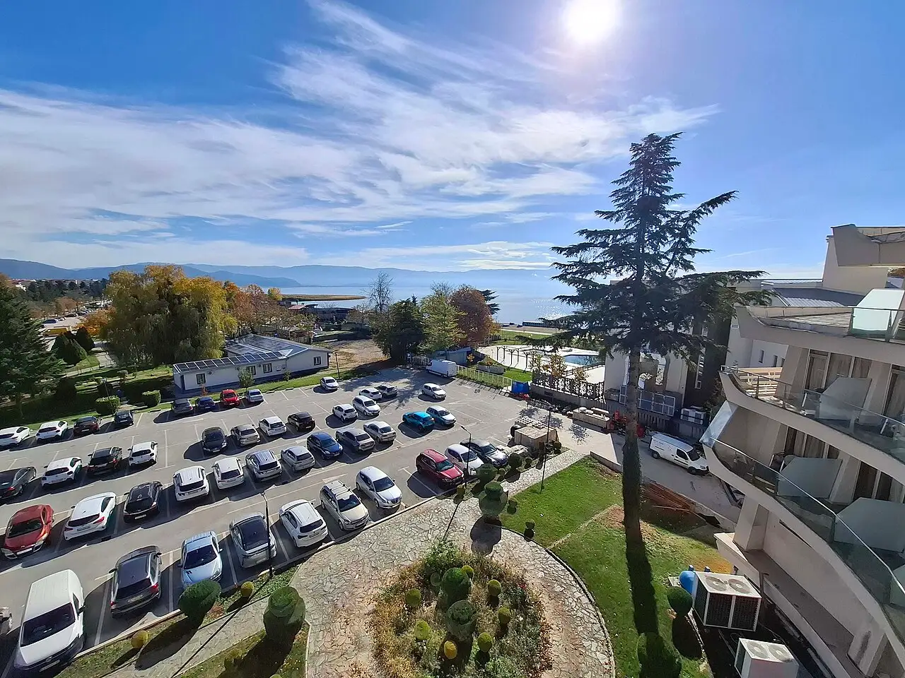 Rows of parked cars in a lakeside hotel car park with Lake Ohrid and distant mountains beyond