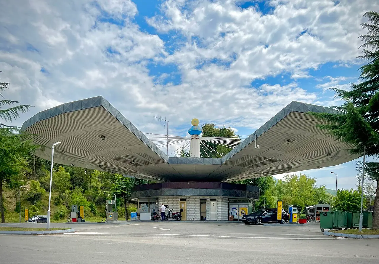 A modernist petrol station with a wide winged concrete canopy near Lake Ohrid, with pumps and parked cars