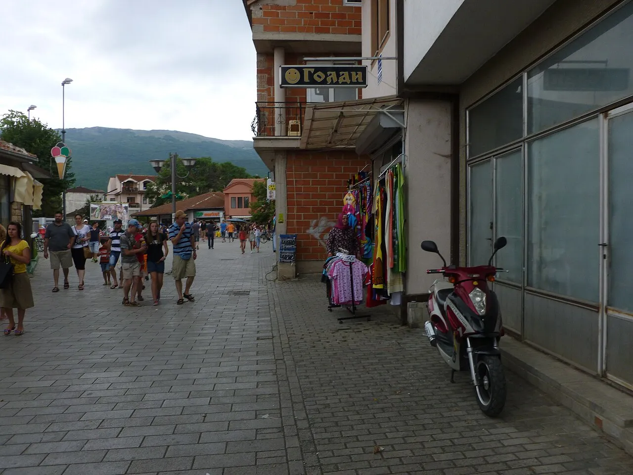 A pedestrianised street in Ohrid with walkers, shopfronts and a scooter parked against a wall
