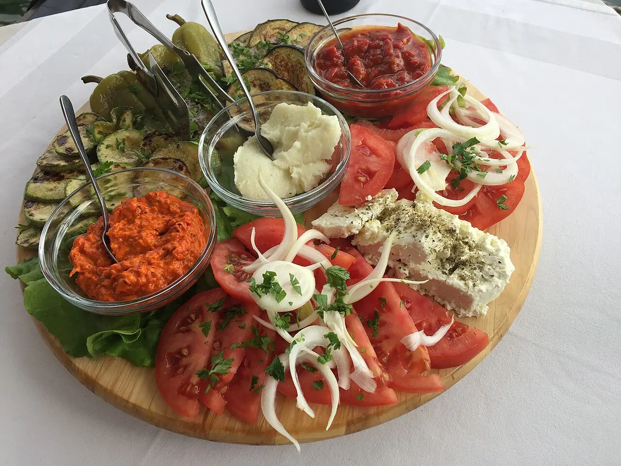 A wooden platter of Macedonian mezze: ajvar, sliced tomatoes, white cheese, grilled vegetables and dips