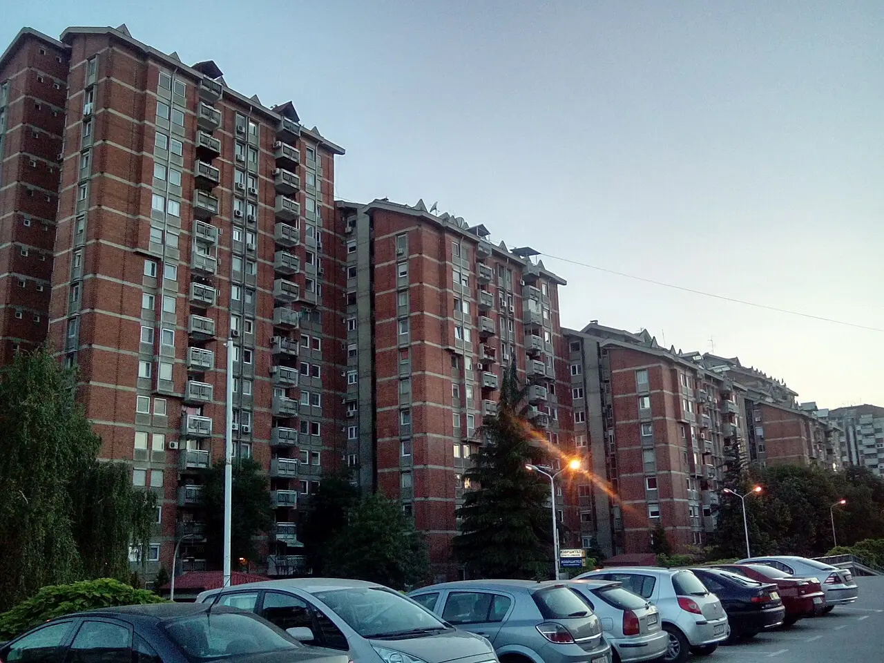 Red-brick residential apartment blocks with balconies and parked cars in central Skopje at dusk