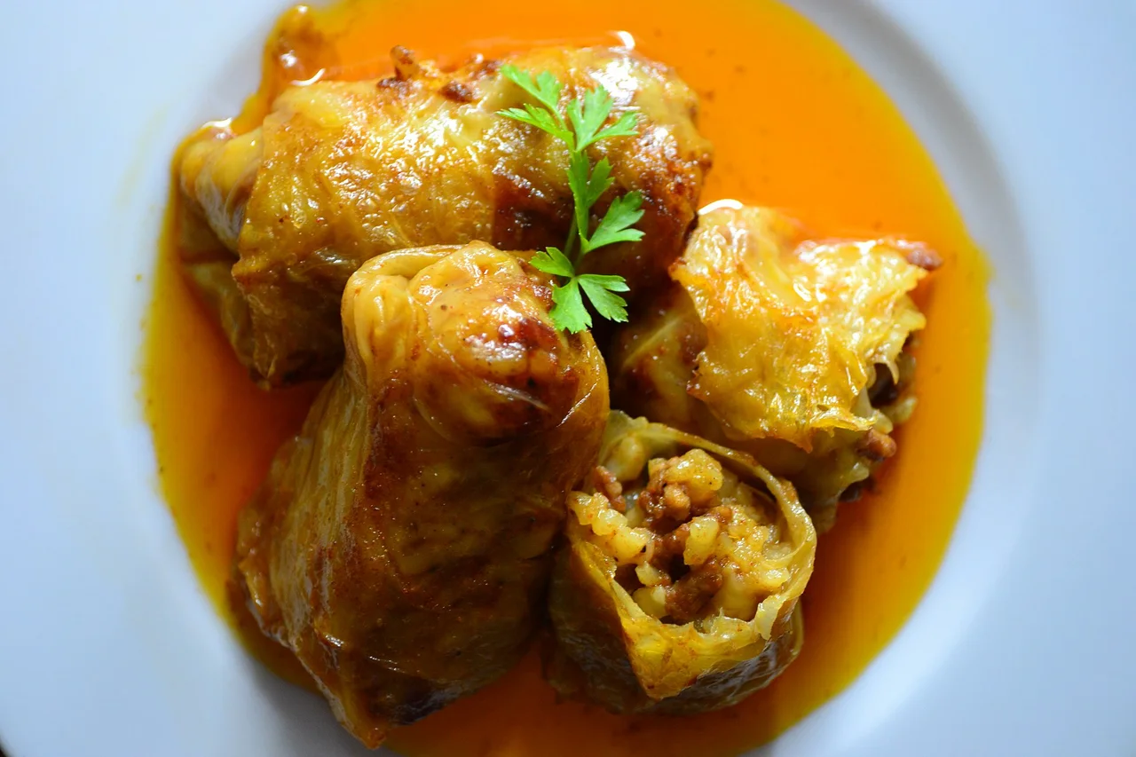 Three cabbage rolls in an orange paprika sauce on a white plate, one split open to show the rice and minced meat filling