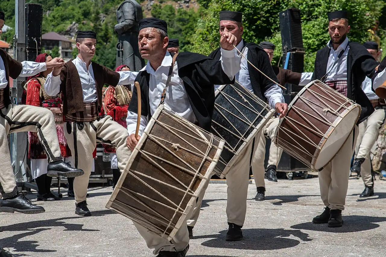 Men in white folk trousers and black vests play large tapan drums with sticks at the Galichnik Wedding