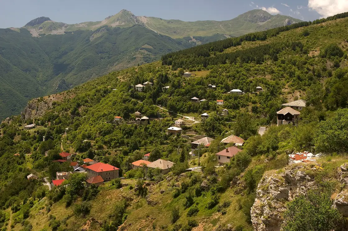 The stone houses of Galichnik village scattered across a green mountainside below the peaks of Mount Bistra