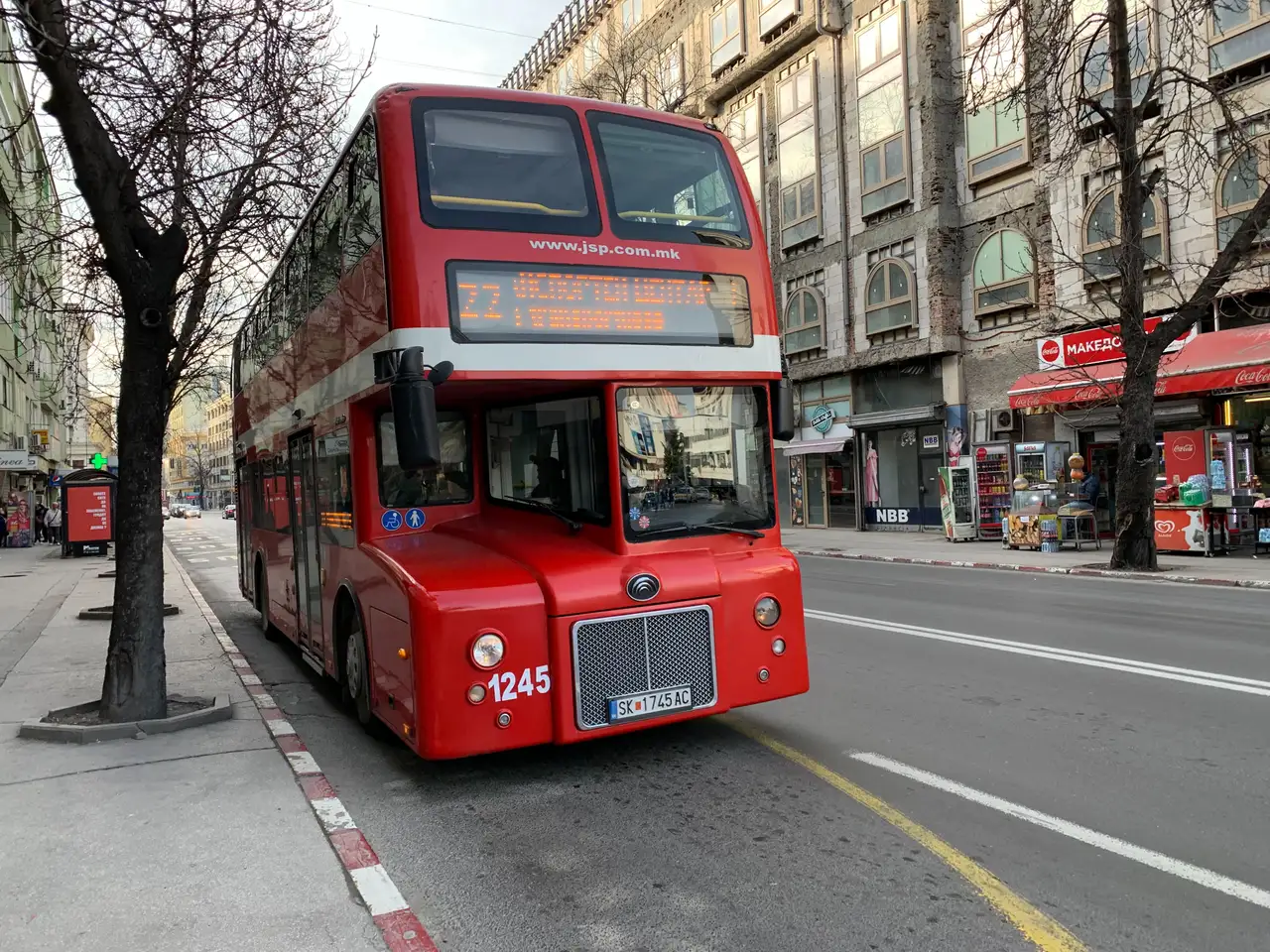 A red JSP city bus on a street in central Skopje