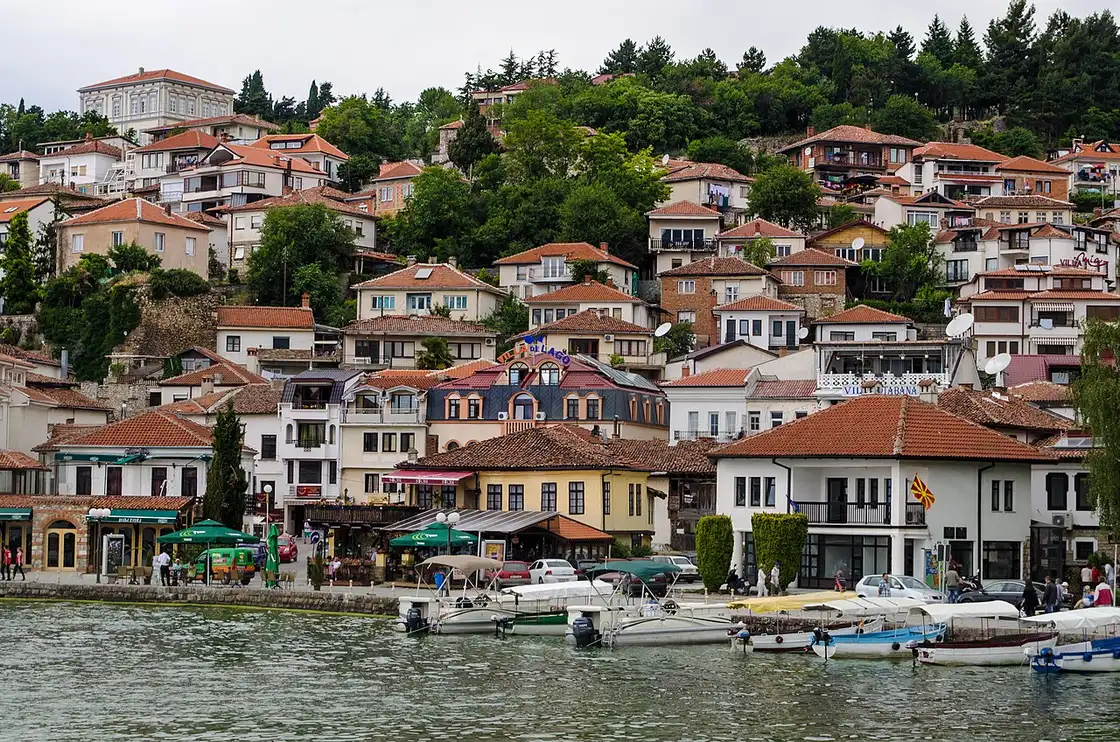 The Ohrid waterfront seen from the lake with tiered old-town houses, cafes and moored boats