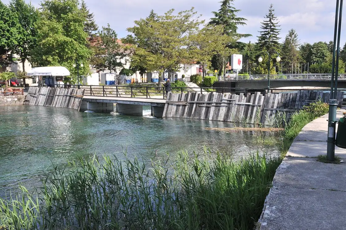 The wooden footbridge over the clear Black Drin in Struga where the river leaves Lake Ohrid, with trees and a riverside walk
