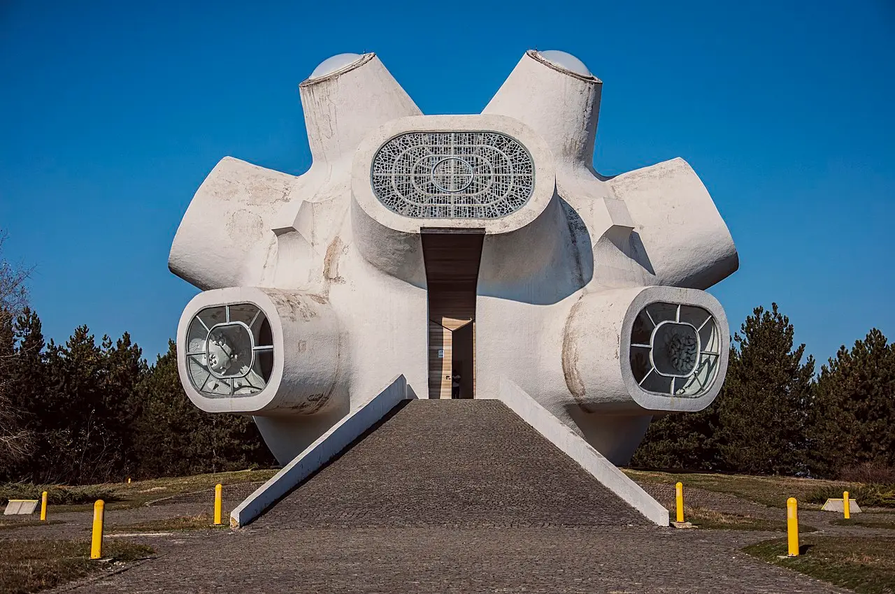 The white spherical Makedonium spomenik with stained-glass windows and bulbous pods, set on a grassy hilltop under a blue sky