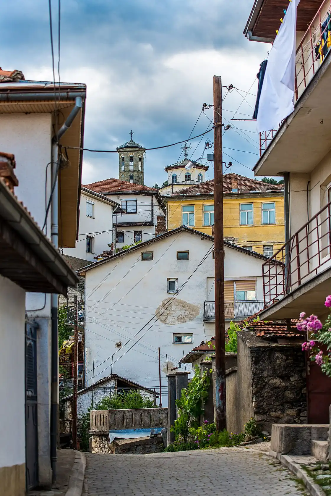 A steep cobbled lane in old Kruševo with white and yellow houses and two church towers rising above the rooftops