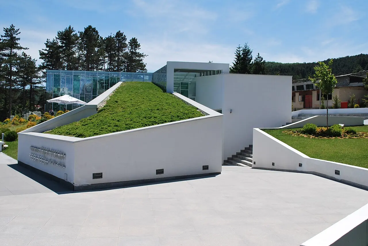 The modern white Toše Proeski Memorial House in Kruševo, with a sloping green grass roof and glass walls set among pines