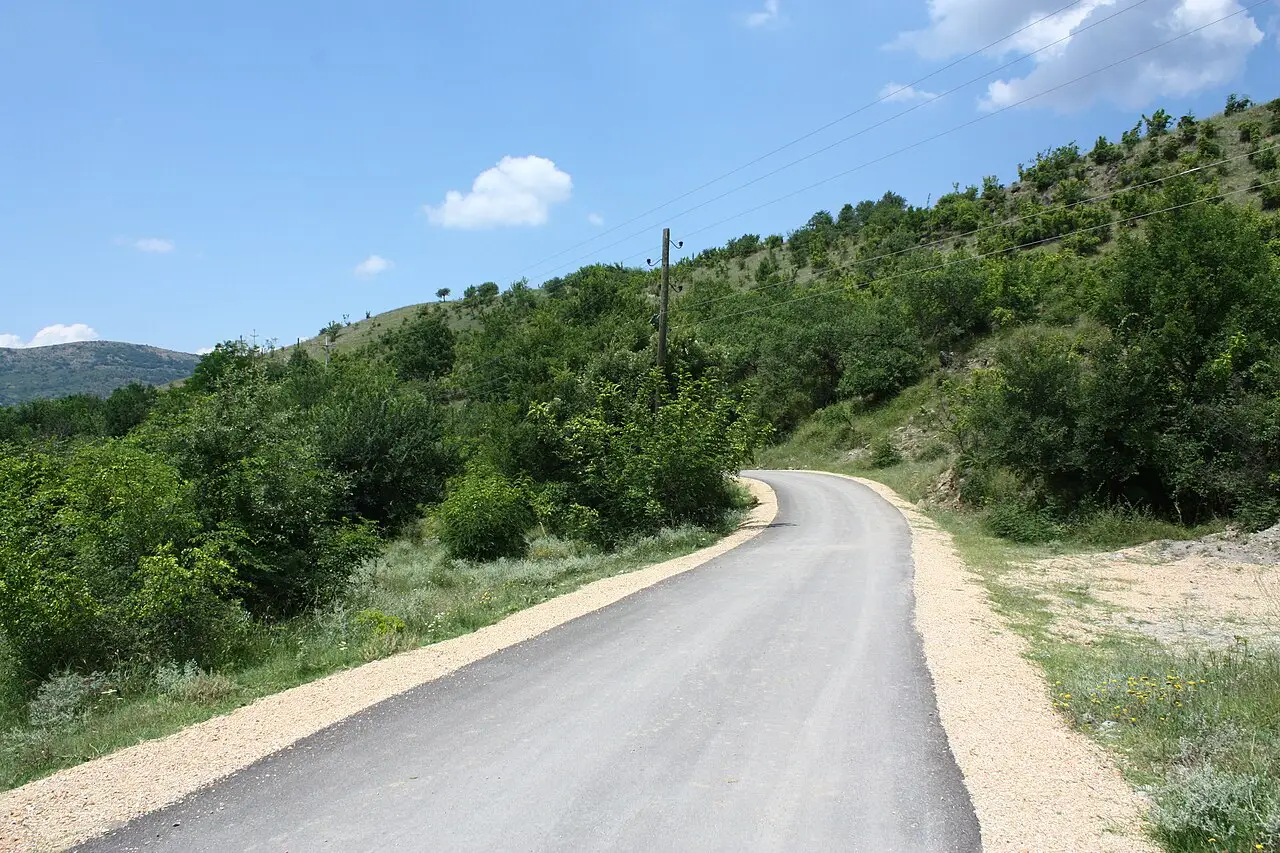 A narrow asphalt road curving through green hills on the way to Kuklica