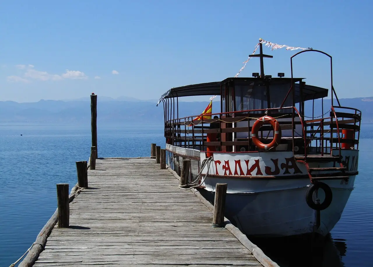 A wooden jetty leading to a traditional excursion boat flying the Macedonian flag on the calm water of Lake Ohrid