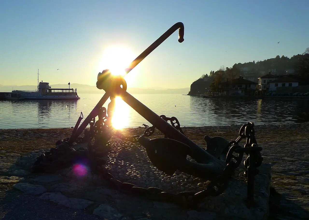 An old ship's anchor monument on the Ohrid shore silhouetted against the sun low over the lake