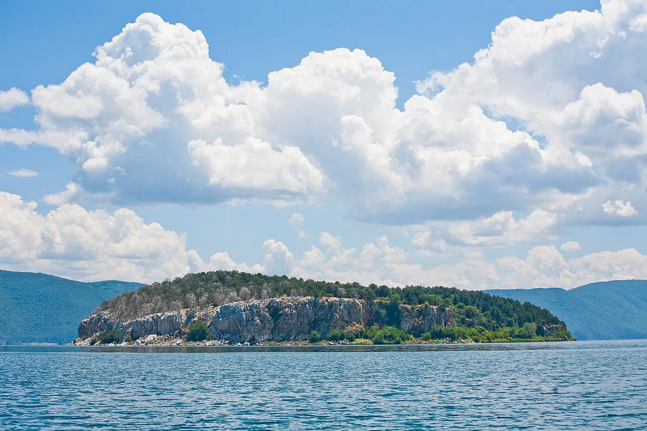 The cliff-ringed, forest-topped island of Golem Grad rising from Lake Prespa under summer clouds