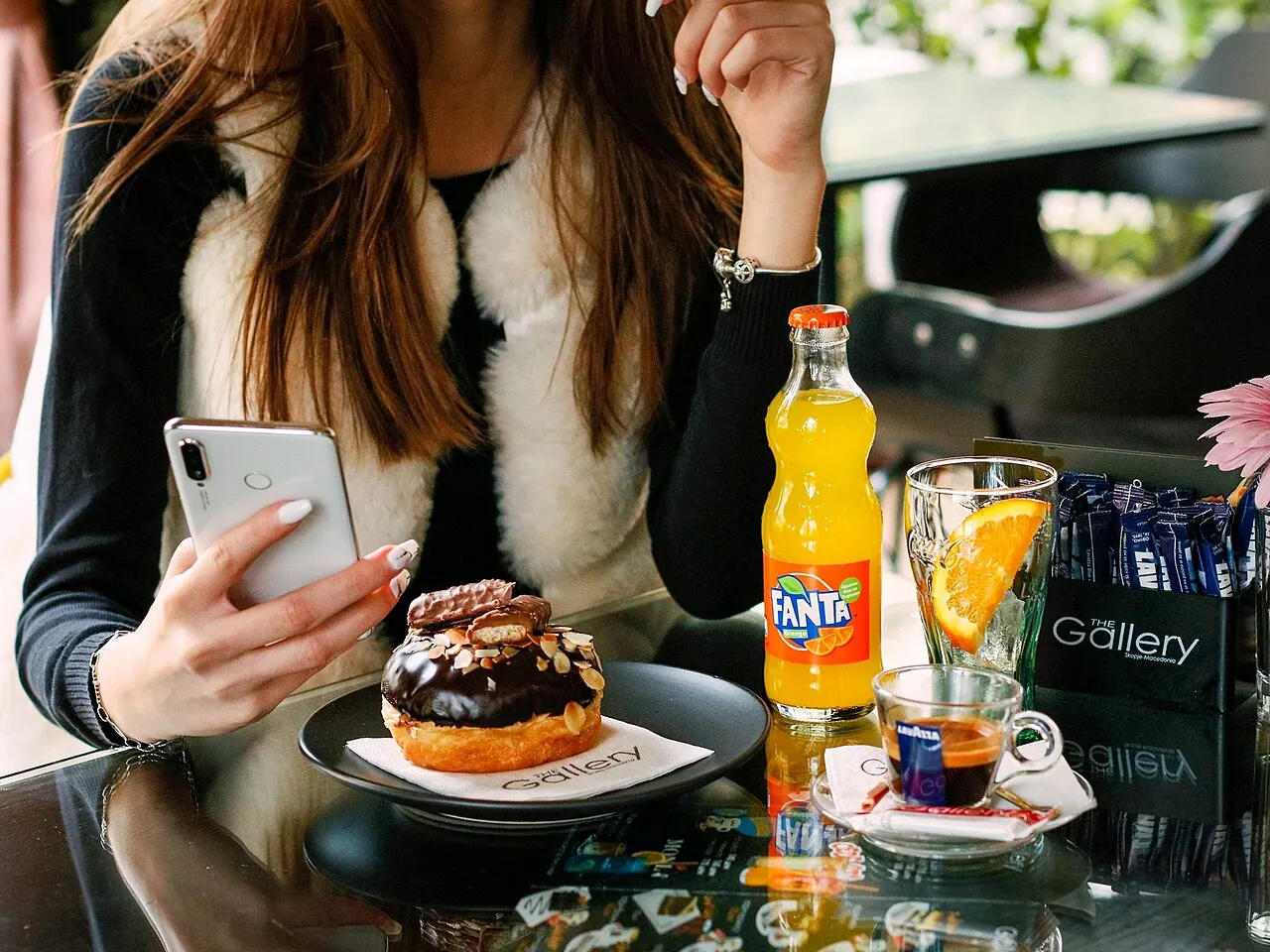 An espresso, a chocolate doughnut and a bottle of Fanta on a glossy café table in Skopje