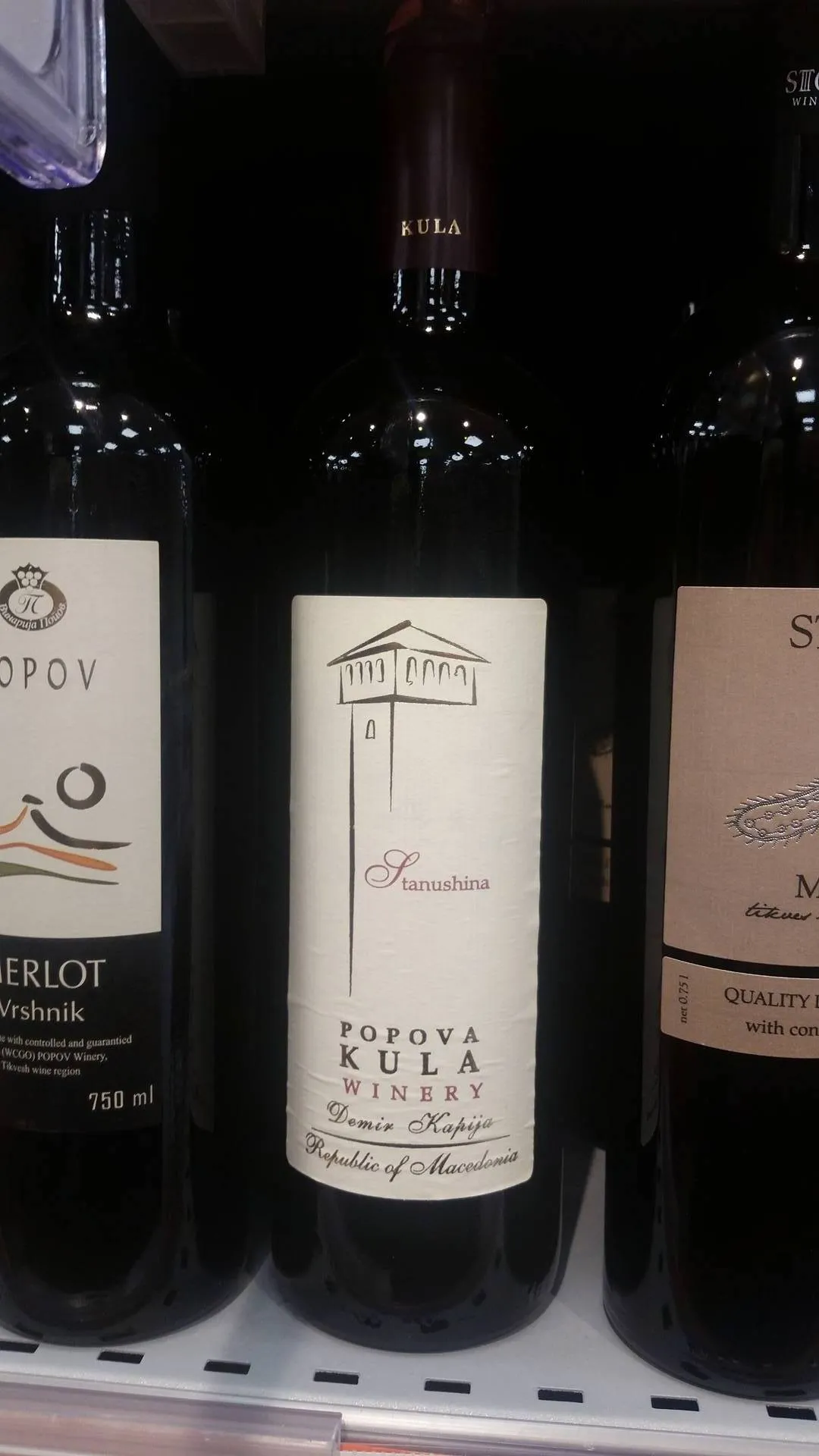 Bottles on a shop shelf including a Popova Kula Stanushina, a Popov Merlot and a Stobi red