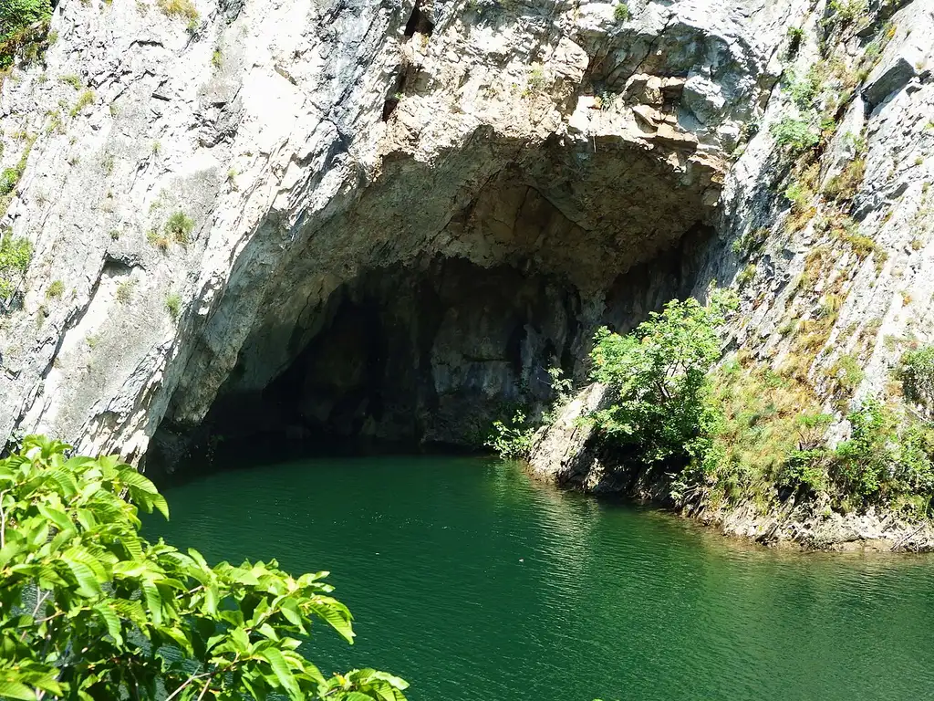 The mouth of a karst cave opening directly onto the green water of the Matka reservoir