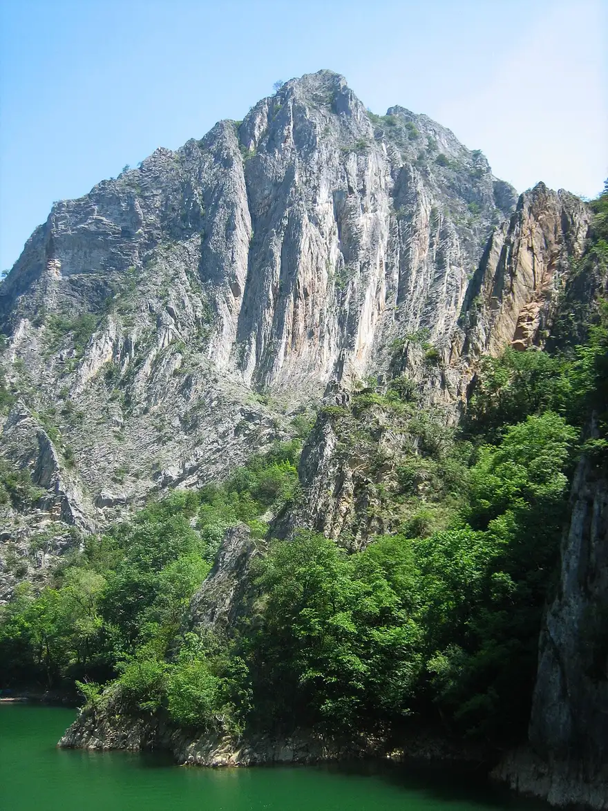 A sheer rock peak towering over the green water of the Matka reservoir