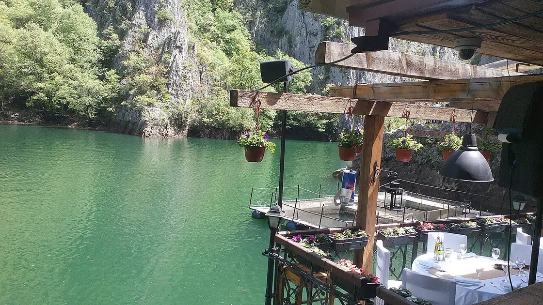 A café terrace with flower boxes and a small floating jetty over the green water of Matka Canyon