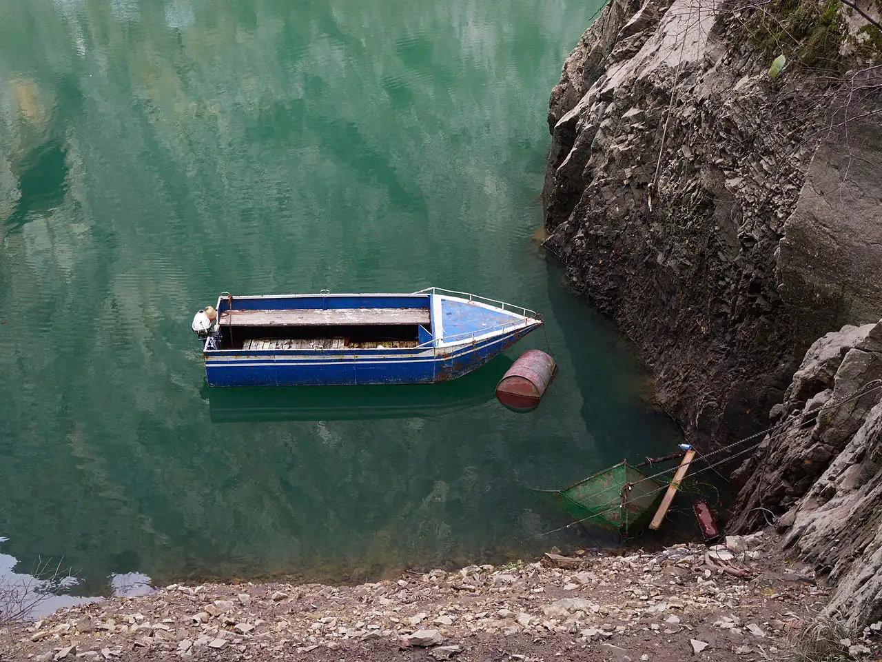 A small wooden boat moored on the emerald water of the Matka reservoir below the cliffs