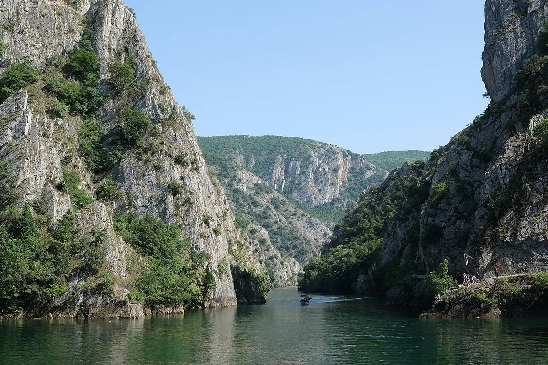 Steep canyon walls dropping into the green reservoir at Matka, seen from a boat