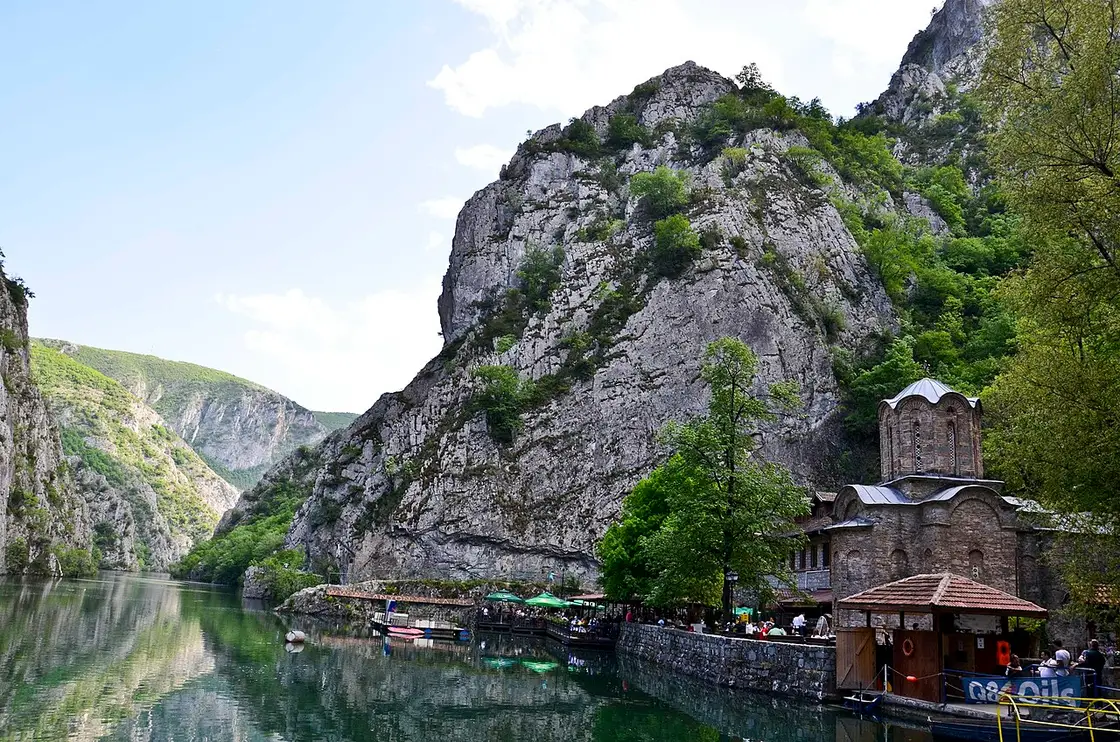 The lakeside St. Andrew monastery church and boats below the cliffs of Matka Canyon