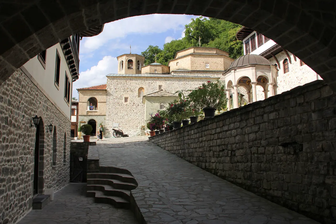 The stone courtyard, church domes and bell tower of Bigorski Monastery seen through an entrance arch