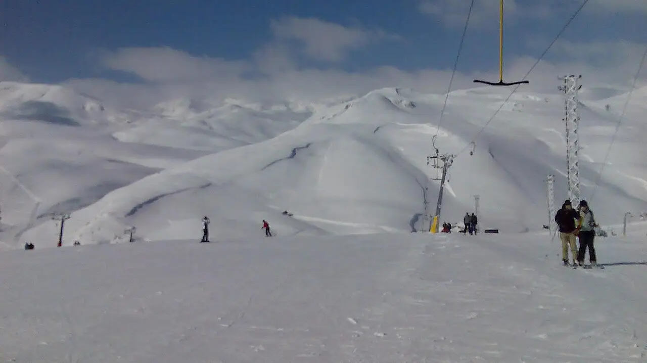 Snow-covered ski slope at Mavrovo with lift pylons and a few skiers under a blue sky