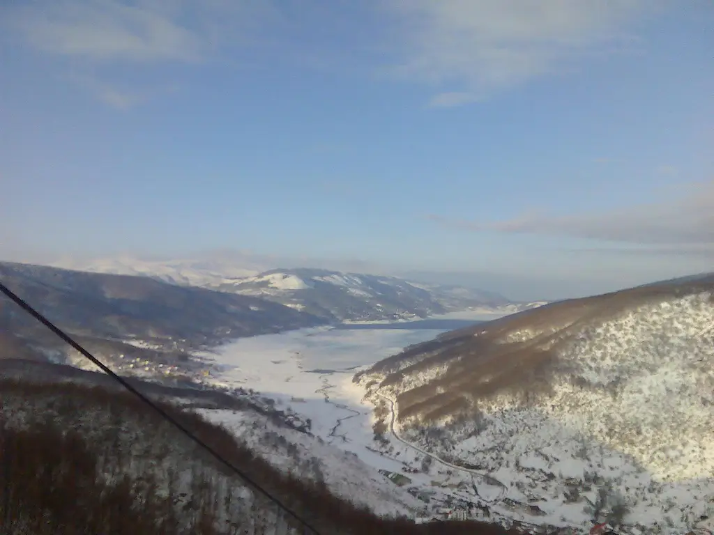 Lake Mavrovo in winter seen from the slopes above, with snow-covered hills around it