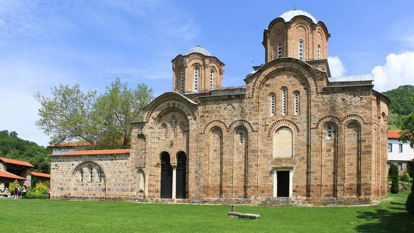 The 14th-century stone and brick church of Lesnovo monastery with its two domes, set on a green lawn under a blue summer sky