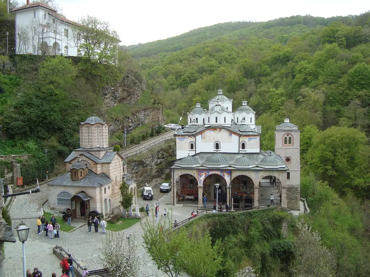 Osogovo monastery from above, the small domed church on the left and the large white church with many green domes and an arcaded porch on the right, in wooded hills