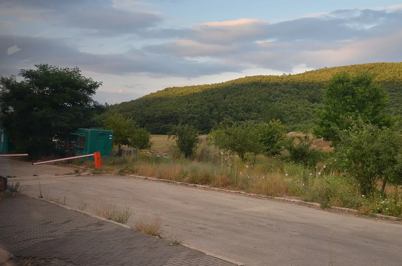 A barrier and small booth at the Kjafasan border crossing between Albania and North Macedonia, with green hills behind