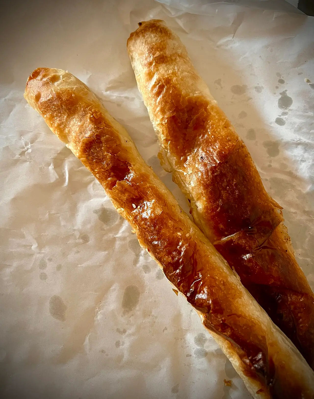 Two golden, freshly baked burek pastry rolls on paper