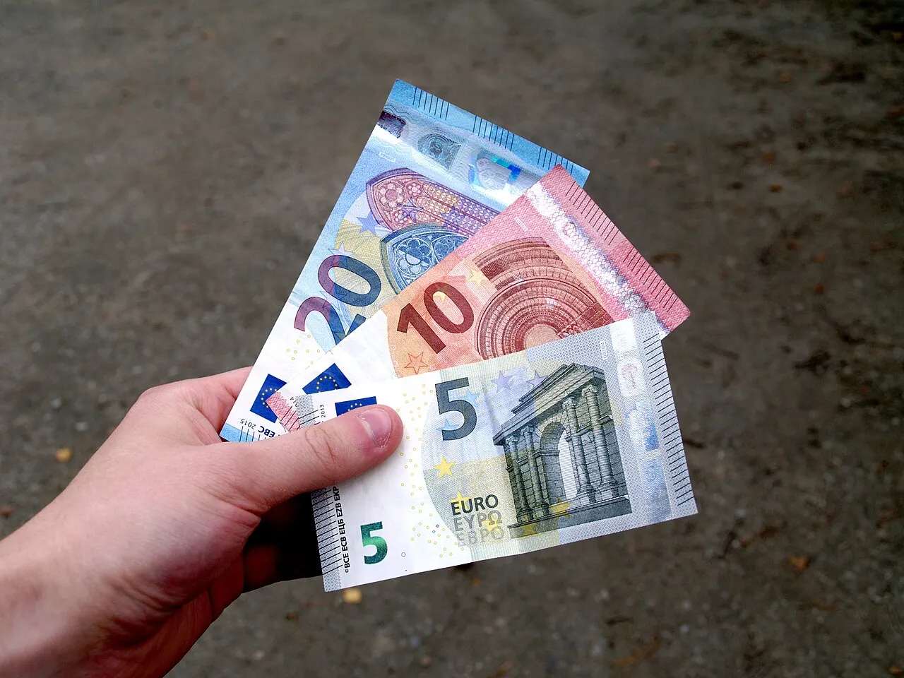 A hand fanning out several euro banknotes of different denominations