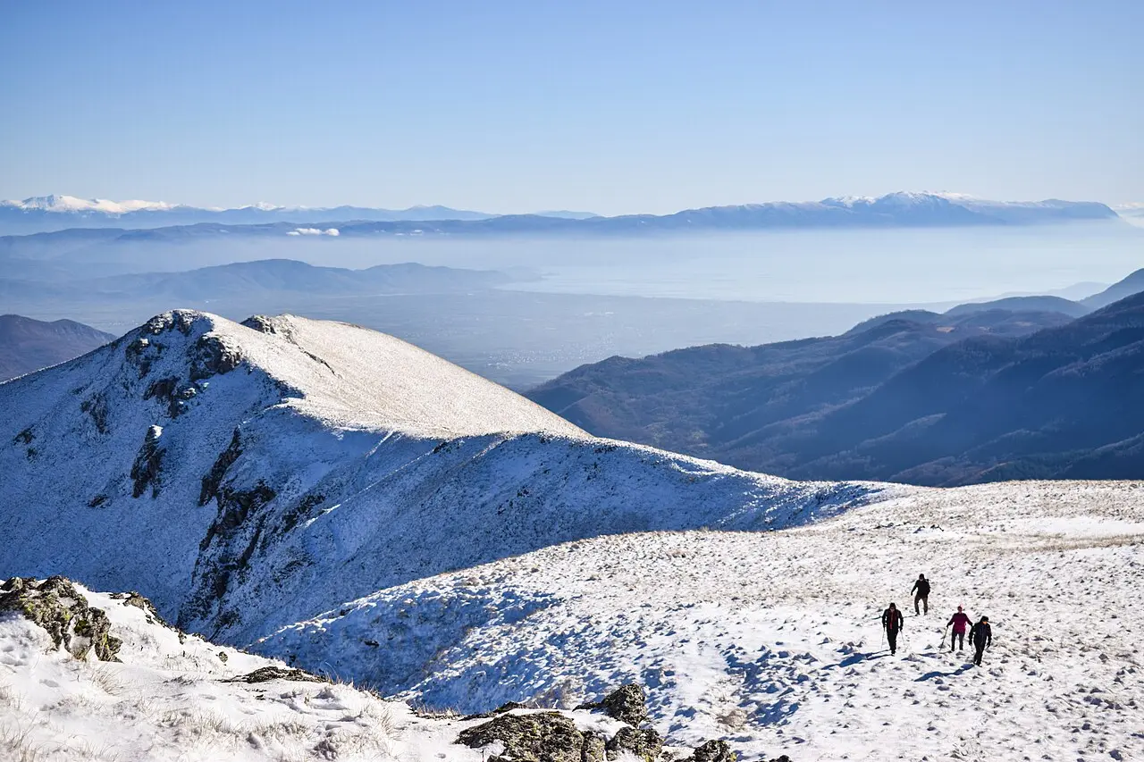 Hikers on a high ridge of Jablanica mountain with the town of Struga and a hazy plain behind
