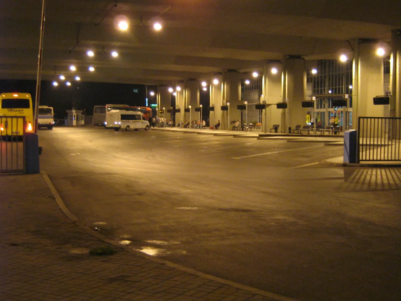 The covered concourse of Skopje's intercity bus station at night with coaches and a minibus